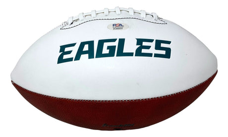 A white and brown Sports Integrity football, signed by Saquon Barkley, features the green EAGLES logo, white laces, and a PSA/DNA authentication sticker near the top.