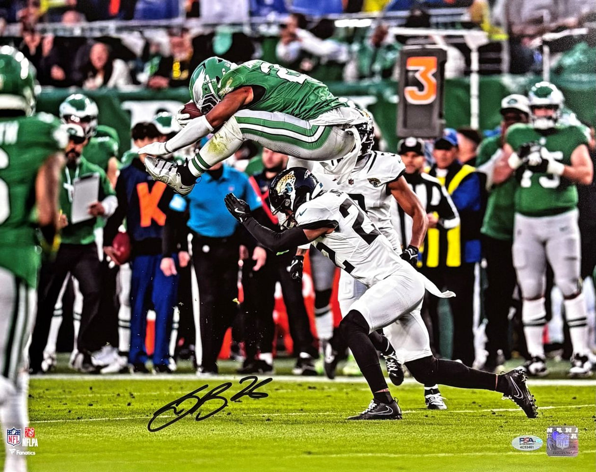 The Sports Integrity Saquon Barkley Signed 16x20 Eagles Reverse Hurdle Color Photo (PSA/DNA ITP) shows Barkley in green leaping over a defender in white during a game, with coaches and refs on the sideline. Signed in black ink at the bottom.