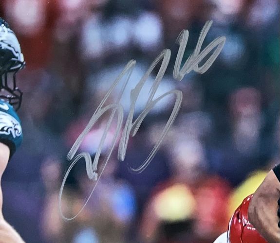 A close-up of the Saquon Barkley Signed Framed 16x20 Eagles Super Bowl 59 Photo by Sports Integrity, featuring a bold silver autograph and Eagles players with a blurred stadium in the background. PSA/DNA authenticated.