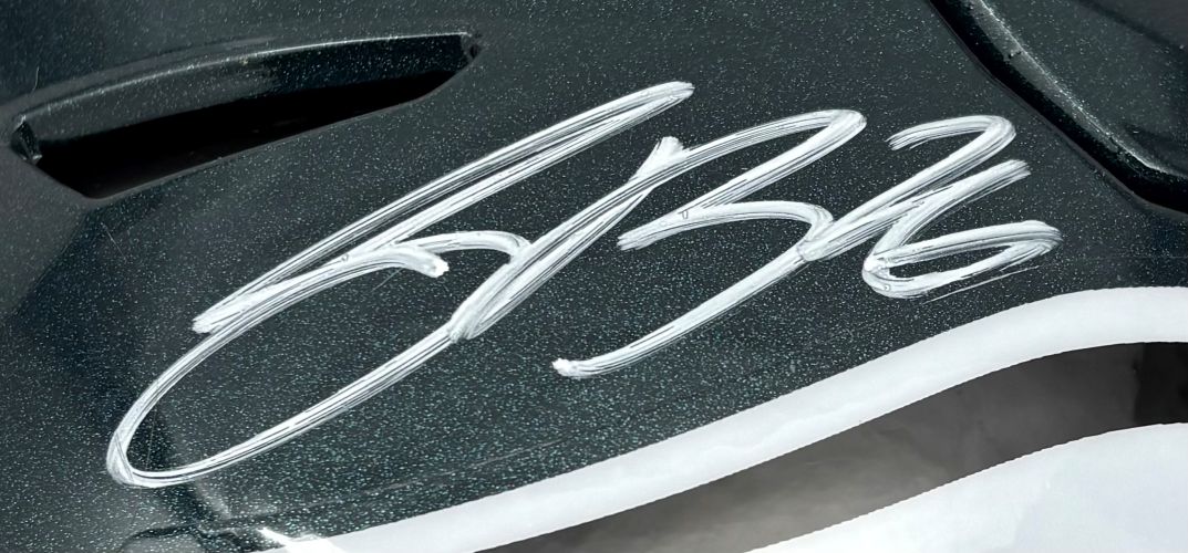 A white Saquon Barkley signature appears on the glossy dark surface of a Philadelphia Eagles FS Authentic SpeedFlex Helmet by Sports Integrity, with part of a curved white shape visible at the bottom.
