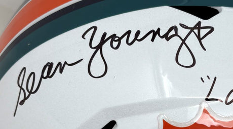 Close-up of a Sports Integrity Sean Young Ace Ventura Dolphins FS Replica Helmet, white with green and orange stripes, featuring a black autograph and "Finkle Laces Out" inscription.
