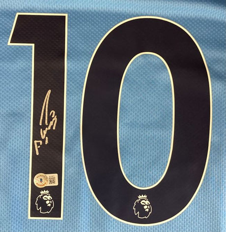 A close-up of a Sergio Aguero Signed Manchester City Puma Soccer Jersey by Sports Integrity, showing a large black number 10 outlined in white, the Premier League lion logo, Aguero's signature, and an authenticity sticker.