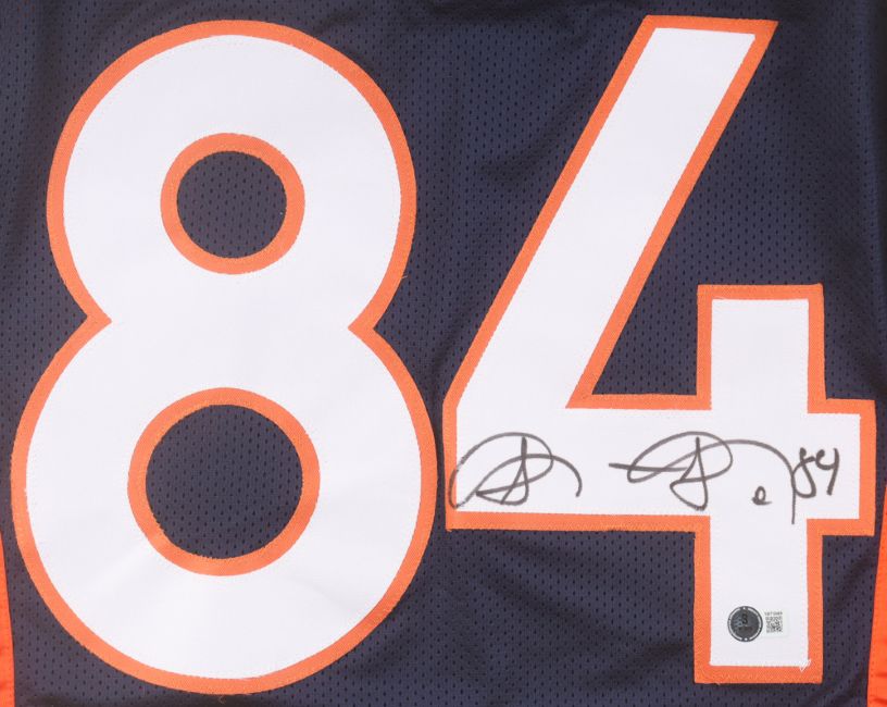The Sports Integrity Shannon Sharpe Denver Navy Pro-Cut Football Jersey features large white and orange number 84, a black marker autograph across the 4, and a BAS authentication sticker below the signature.