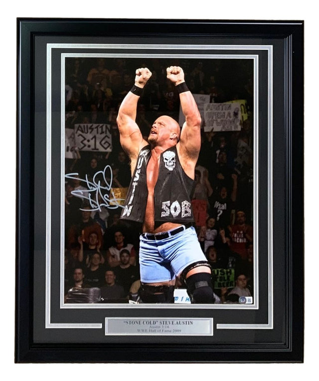 The Sports Integrity Stone Cold Steve Austin Signed Autographed Framed 16x20 WWE Photo BAS features the wrestler in the ring, arms raised, wearing a black vest and blue shorts, with cheering fans and signs in the background.