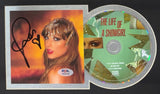 A Taylor Swift Signed Framed Insert with an 8x10 "Life Of A Showgirl" photo, PSA/DNA authenticated by Sports Integrity, is shown next to the CD. Part of her face is reflected on the CD.