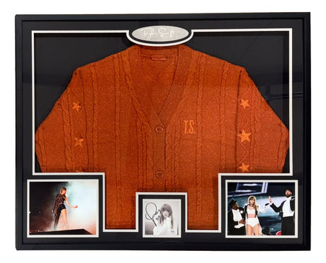 The Sports Integrity Taylor Swift Signed Framed Life Of Showgirl Cardigan Sweater w/ Signed Insert (PSA/DNA) features an orange cardigan with T.S. and stars, Taylor’s signature, and three photos of her performing, posing, and singing on stage.
