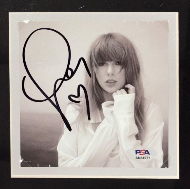 Black-and-white photo of Taylor Swift wearing a loose white shirt, holding her collar. Includes a large autograph and PSA/DNA authentication. Product: Taylor Swift Signed Framed Life Of Showgirl Cardigan Sweater w/ Signed Insert by Sports Integrity.