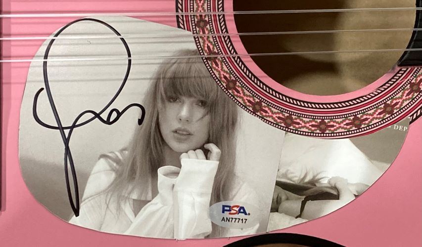 A bold, black-autographed black-and-white photo of Taylor Swift is attached near the sound hole of a Sports Integrity 38" Tortured Poets Department pink acoustic guitar, PSA authenticated with holo sticker.