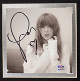 A Taylor Swift Framed Tortured Poets Department Shirt by Sports Integrity, featuring a signed insert authenticated by PSA/DNA, showcases her black-and-white photo with a large autograph and heart symbol.