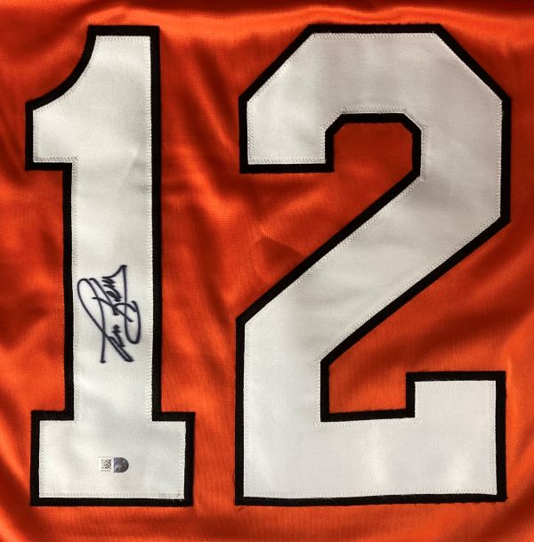 A Tim Kerr Philadelphia signed orange hockey jersey by Sports Integrity features a large white number 12 outlined in black with his signature in black ink on the left side.