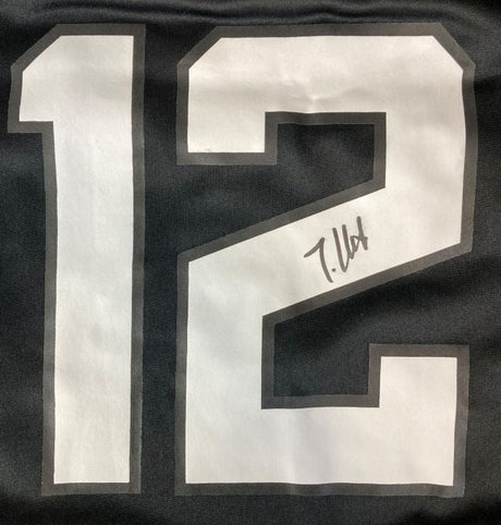 A close-up of a Travis Hunter Signed Jacksonville Jaguars Black Nike Game Replica Jersey by Sports Integrity, featuring a large white number 12 outlined in gray and a black ink signature on the number 2.