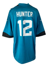 A teal Jacksonville Jaguars Nike Game Replica Jersey by Sports Integrity, featuring HUNTER and #12 in white on the back, with Travis Hunter's autograph below the number.