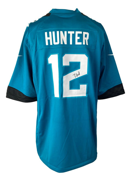 A teal Jacksonville Jaguars Nike Game Replica Jersey by Sports Integrity, featuring HUNTER and #12 in white on the back, with Travis Hunter's autograph below the number.