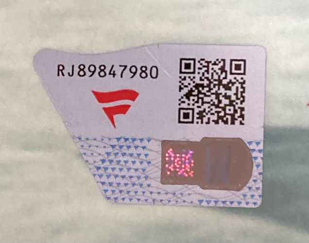 A security sticker for the Trish Stratus Signed Framed 8x10 WWE Photo vs Lita by Sports Integrity features a QR code, serial RG89847980, a red F logo, and a holographic pink-patterned square on pale blue.