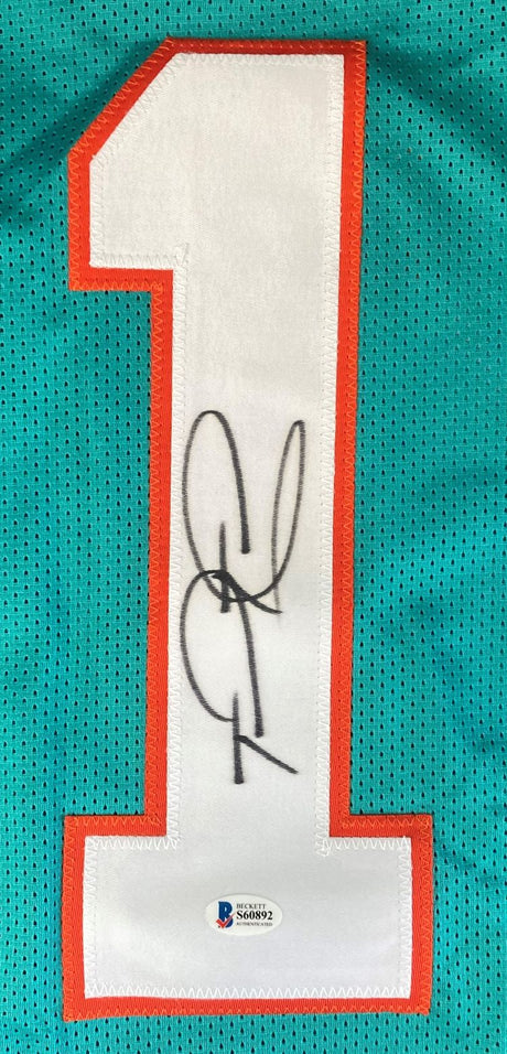 The Sports Integrity Tua Tagovailoa Miami Signed Teal Football Jersey features a large white number 1 outlined in orange, black autograph on the number, and a BAS authentication sticker near the bottom.