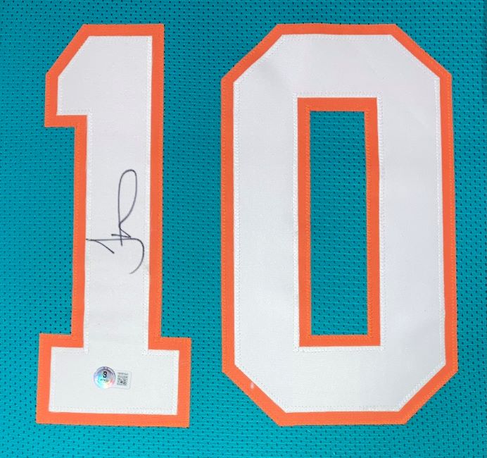 This Tyreek Hill Miami custom teal football jersey from Sports Integrity features large white and orange number 10, the number 1 signed in black ink with a BAS ITP authenticity sticker below the signature, and comes framed.