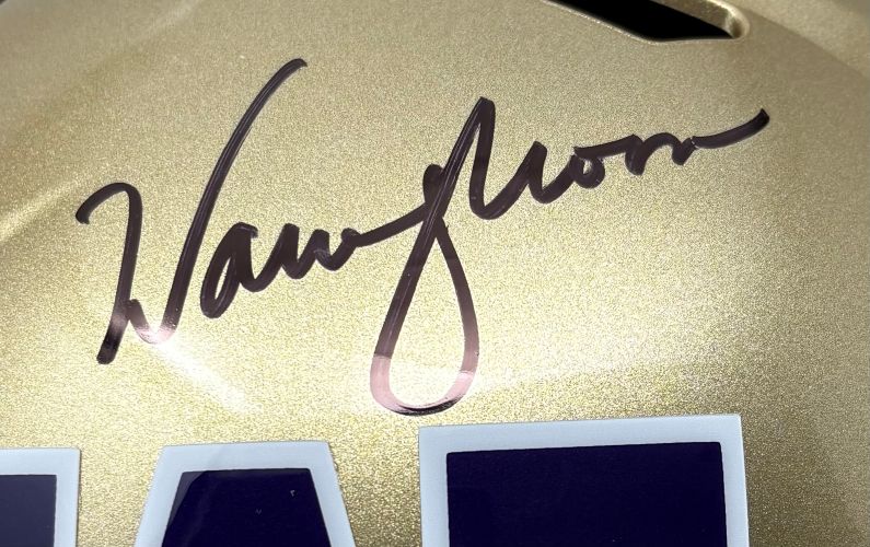 A close-up of a Warren Moon Signed Washington Huskies Full Size Speed Replica Helmet by Sports Integrity, showing a black autograph and part of the blue and white numbering at the bottom.