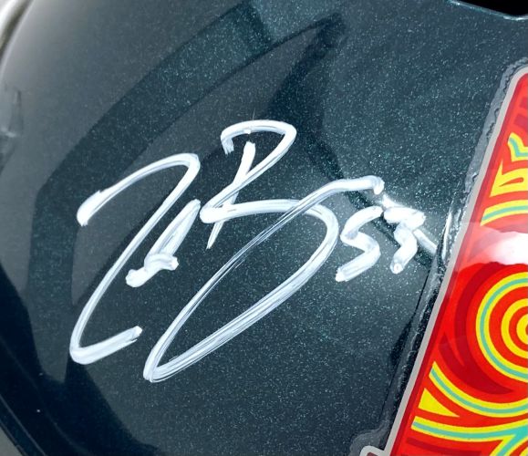 A close-up of a Zack Baun Signed Philadelphia Eagles FS Super Bowl 59 Speed Replica Helmet by Sports Integrity, featuring a white autograph and "33," beside a colorful sticker with red, yellow, and green circular patterns.