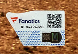 A close-up of a Fanatics authentication sticker with the logo, QR code, and code QL84426628 on a Zack Wheeler Signed Framed 16x20 Philadelphia Phillies Photo by Sports Integrity, set against a blurred brown surface.